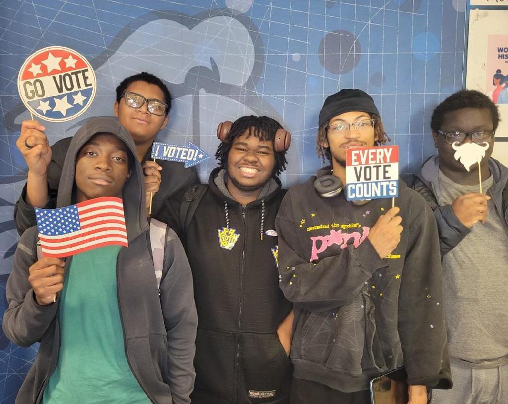 Group of young people holding signs and an American flag promoting voting and civic engagement.