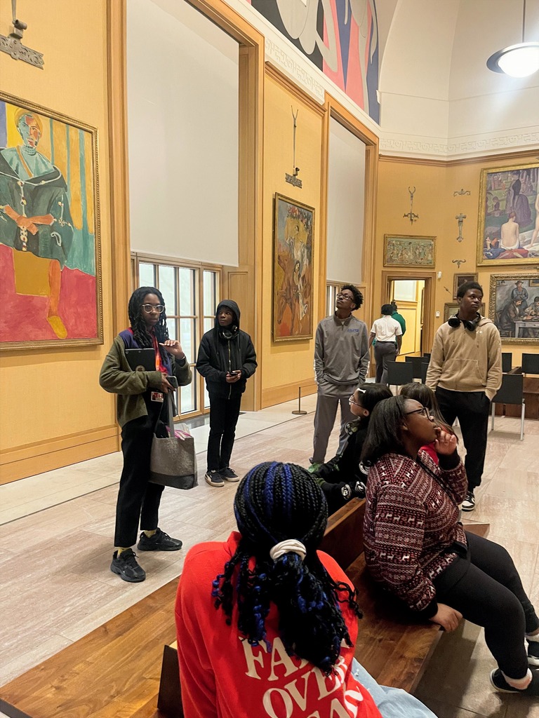 Group of young people exploring an art gallery with large colorful paintings on the walls and natural light from tall windows.