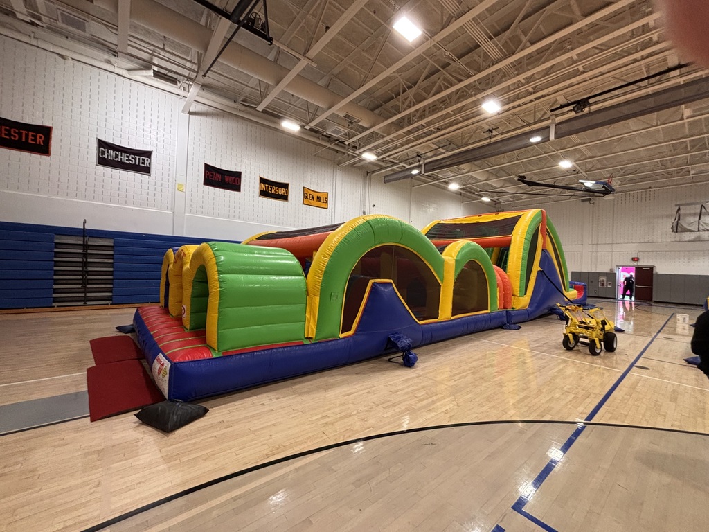 Colorful inflatable obstacle course stretches across a gym floor, ready for participants to race through.