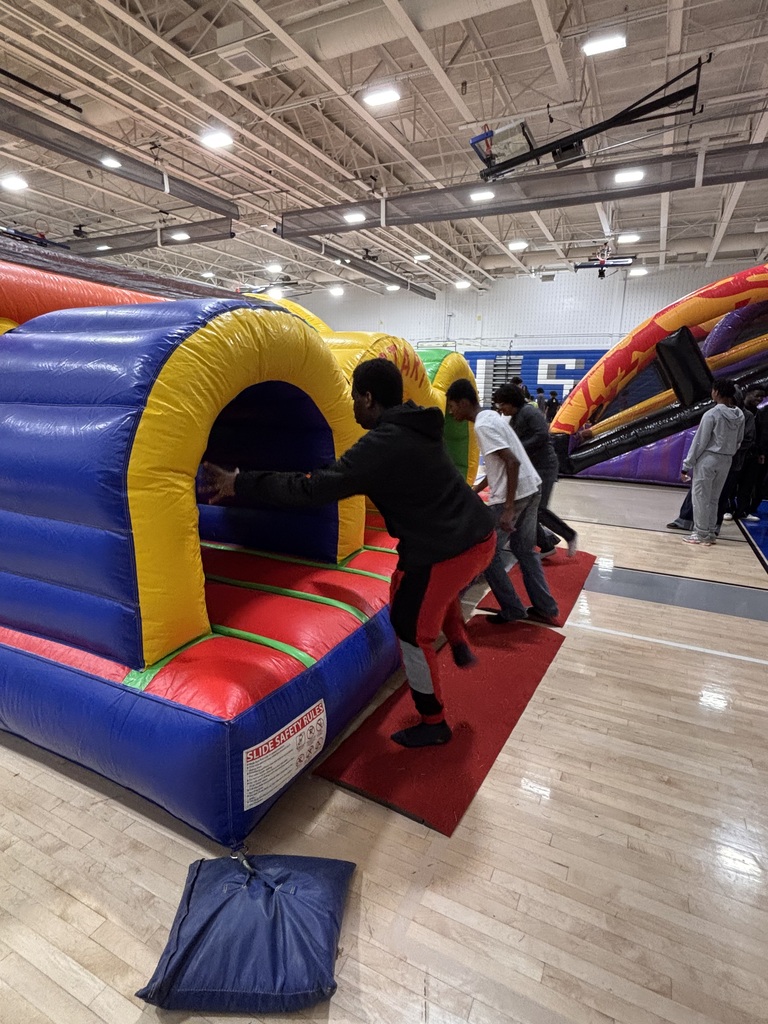 Students enter a colorful inflatable obstacle course during a school event held in a gymnasium.