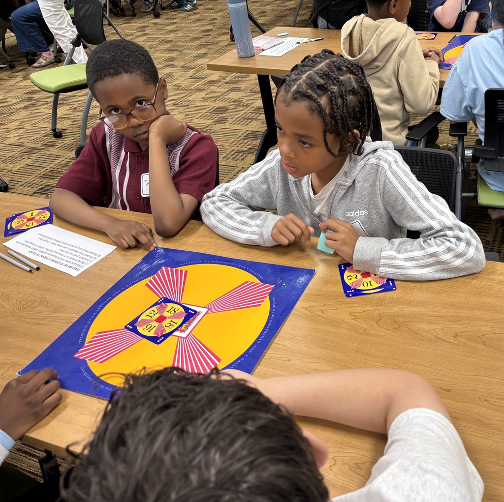 Students collaborate around a table during a Math 24 Challenge competition, studying number cards and game boards.