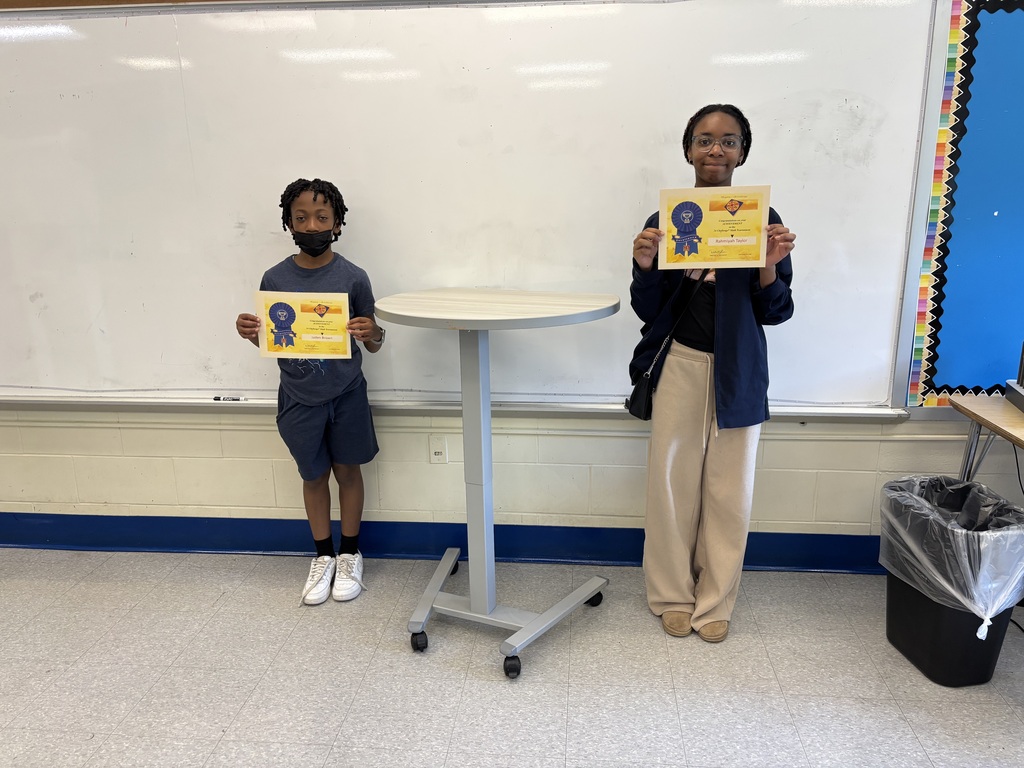 Two students stand in a classroom holding achievement certificates earned through the Math 24 Challenge competition.