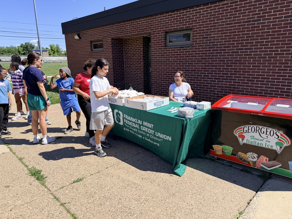 People lined up outdoors at a community event receiving food from a table with Franklin Mint Federal Credit Union branding.