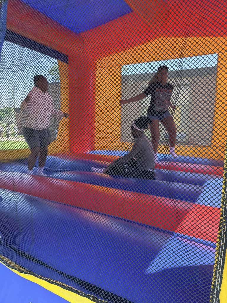 Three children playing and jumping inside a colorful inflatable bounce house on a sunny day.