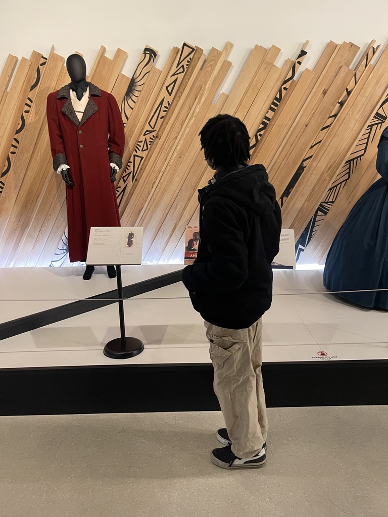 Student examines a historic red coat displayed on a mannequin as part of a museum exhibit on African American history and culture.