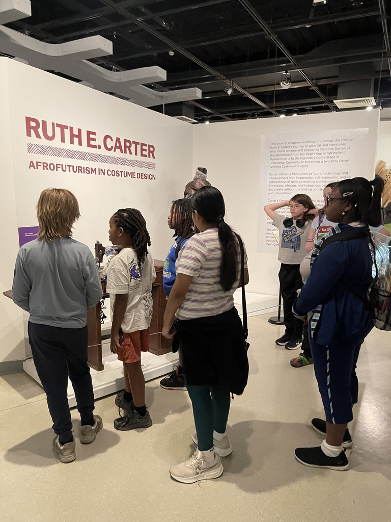 Students gather around an exhibit titled “Ruth E. Carter: Afrofuturism in Costume Design,” learning about costume design and cultural storytelling.
