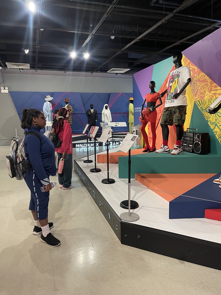 Student observes a colorful fashion exhibit showcasing modern clothing, accessories, and cultural influences in costume design.
