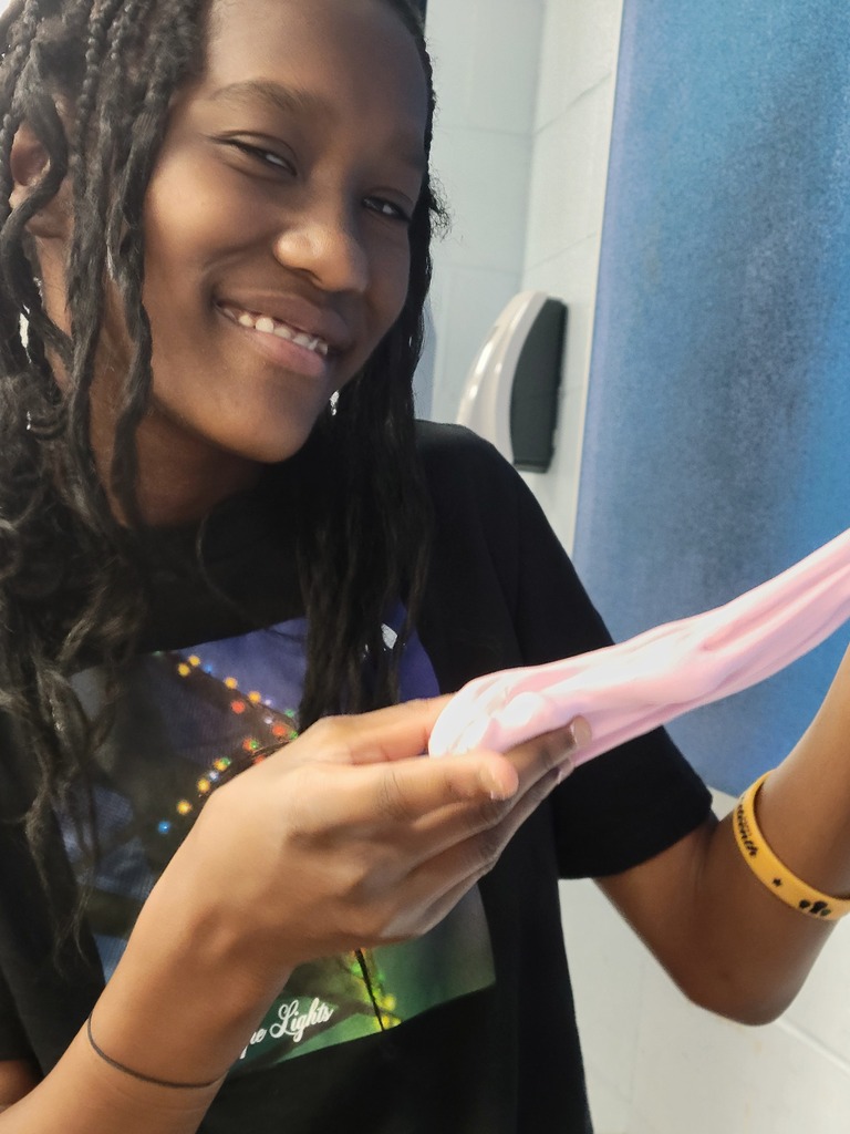Smiling student stretching pink slime with both hands in a bright room.