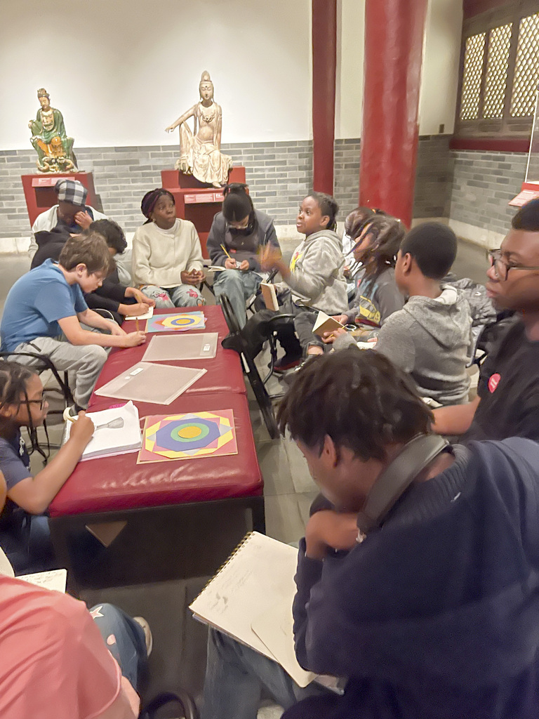 A group of students sketching and discussing art inside a museum with statues in the background.