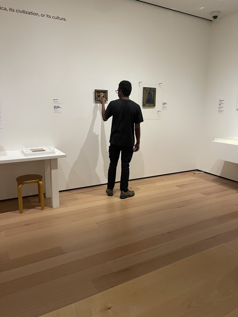 Man in black shirt closely examining a small framed artwork on a white gallery wall.