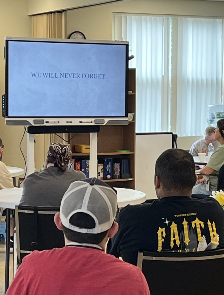 A room of young adults at tables watching a video on a large television