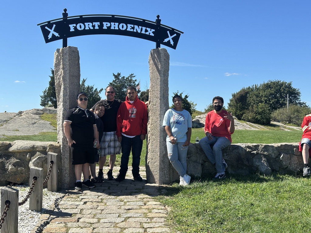 Men and women standing outdoors at a stone entrance to Fort Phoenix