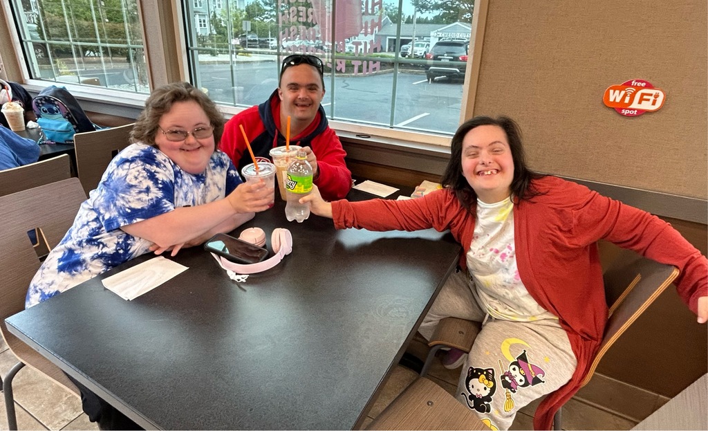 A group of men and women smiling, sitting in a booth holding up coffee drinks 