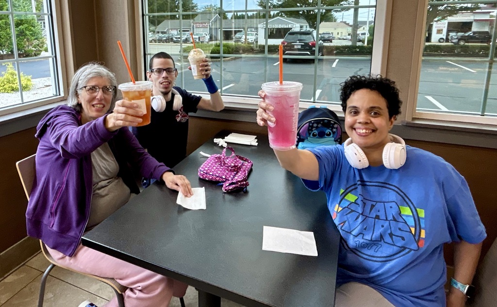 A group of men and women smiling, sitting in a booth holding up coffee drinks 