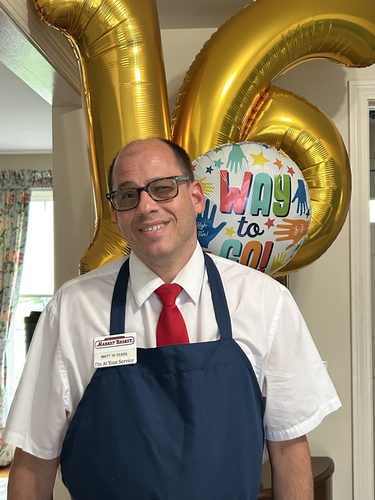 Man in work uniform poses in front of celebratory balloons.