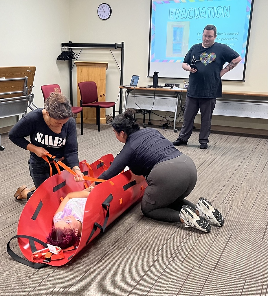Man observes two women fastening another woman into a med sled 