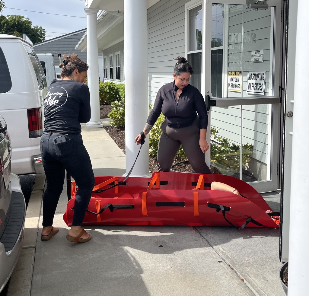 Two women pulling a med sled out of a building 