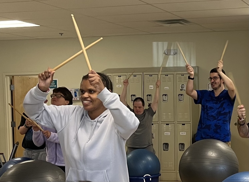 A group of men and women playing drums using a large plastic container and an exercise ball
