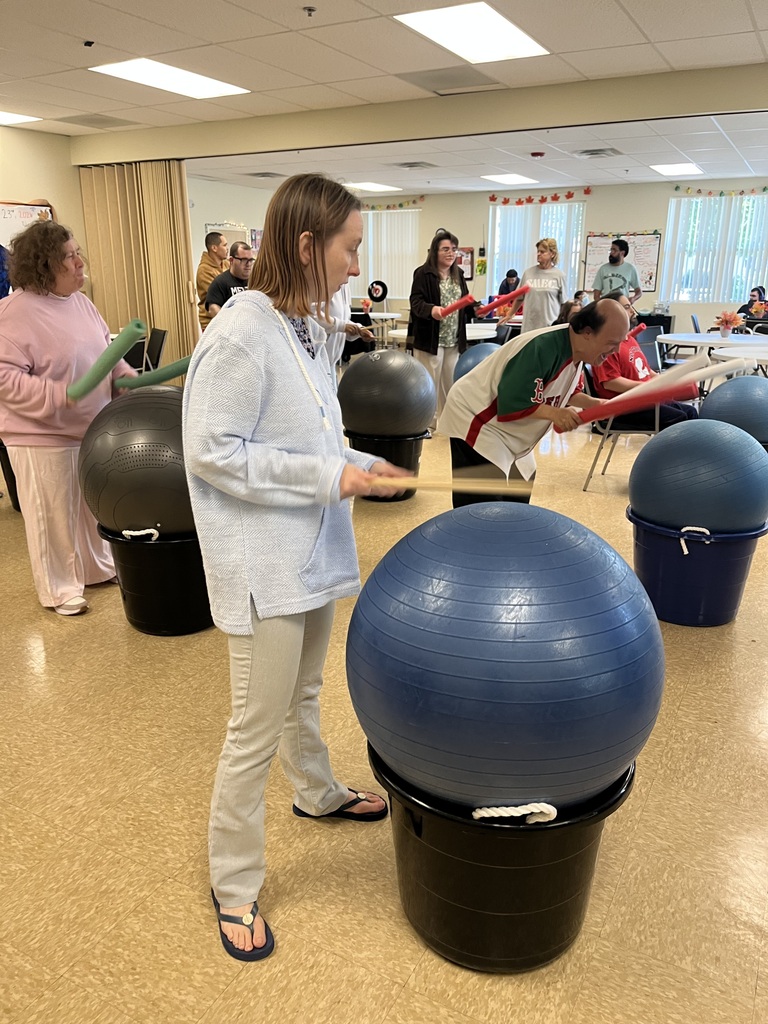 A group of men and women playing drums using a large plastic container and an exercise ball