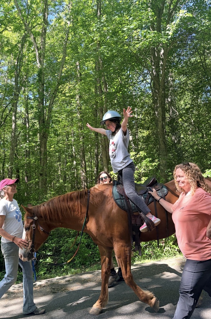Woman with arms spread open riding a horse with handlers alongside 