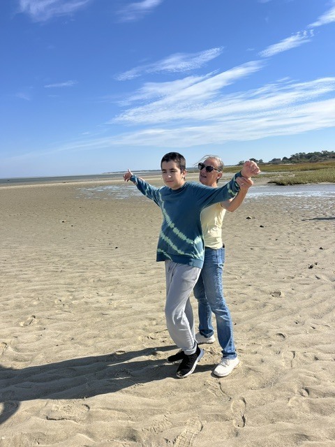 A teacher holding a students arms out like they are flying.  The are standing on a sandy beach.