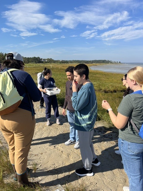 Students and staff members on the beach getting ready to explore a bin that is being held by a staff member.