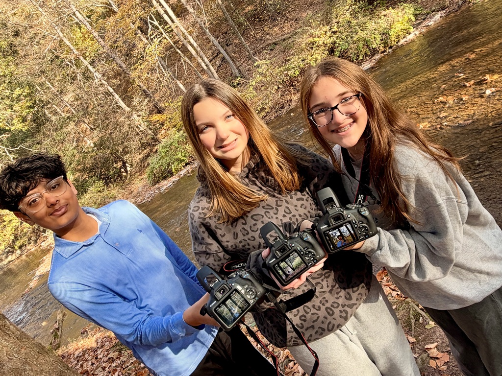 students holding cameras beside a creek
