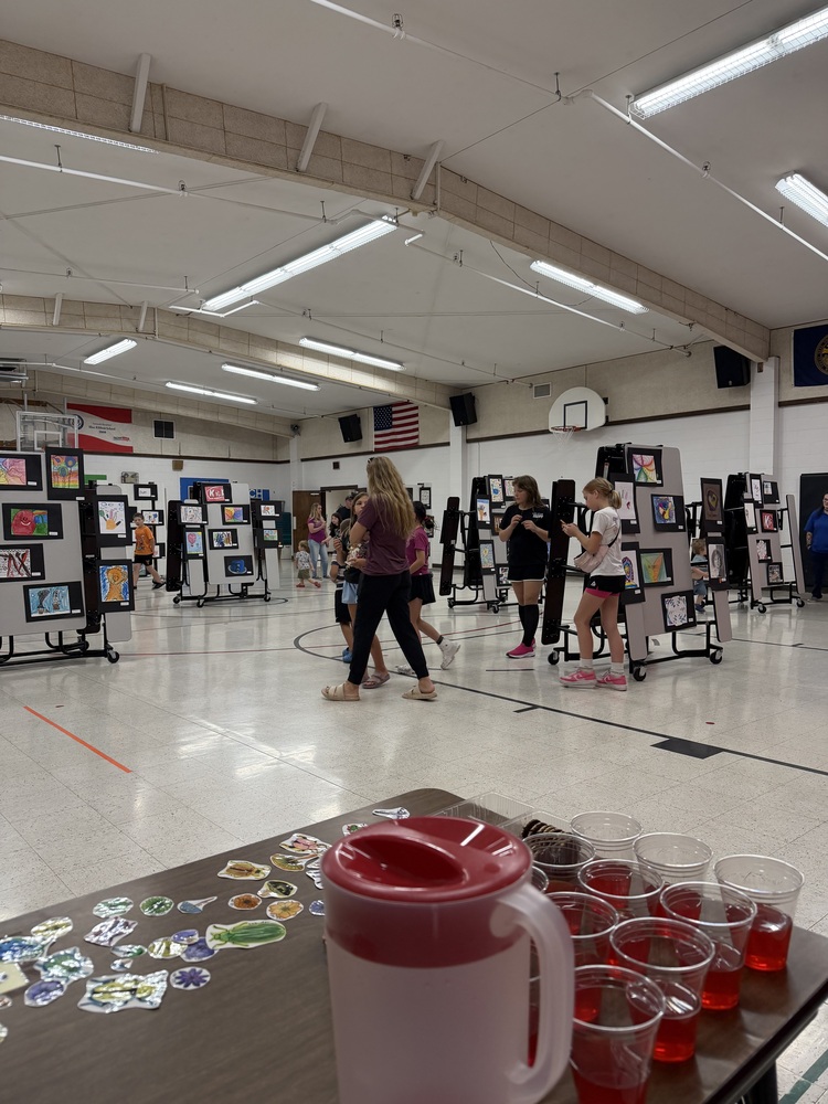 Parents and children walking through the art gallery of elementary artwork displayed on lunch tables.