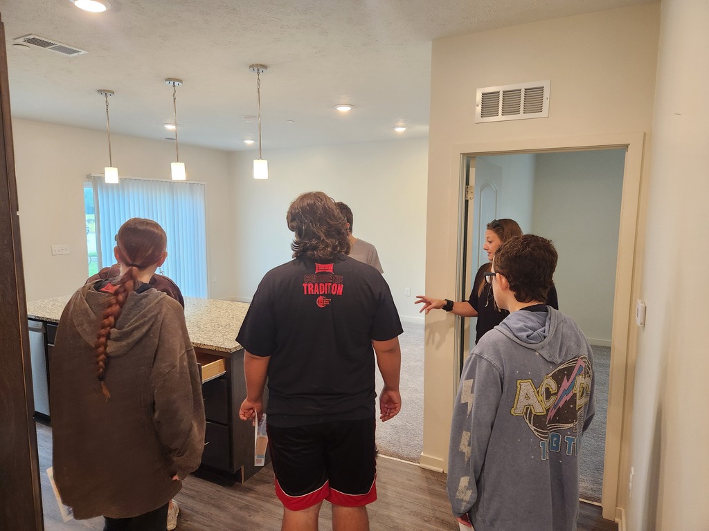 3 students looking at and listening to Amanda tell them about what the kitchen has to offer in their apartment complex.