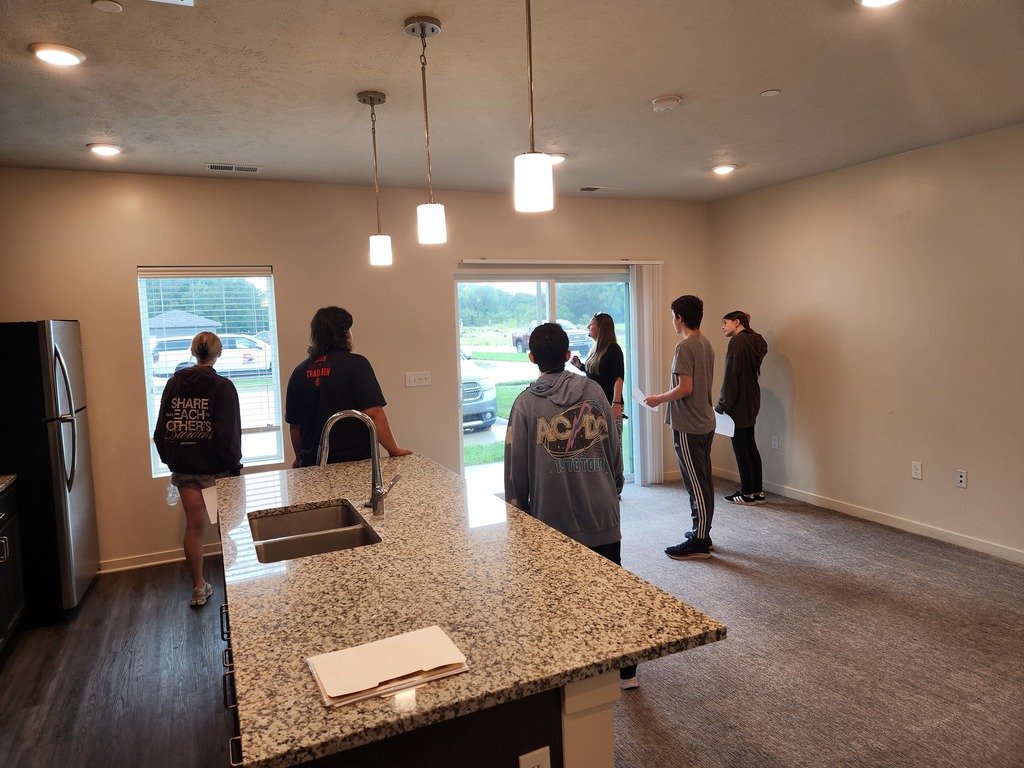 5 students learning from Amanda about the amenities of the Heartland Apartment Complex. They are standing in a modern dining area of an apartment.
