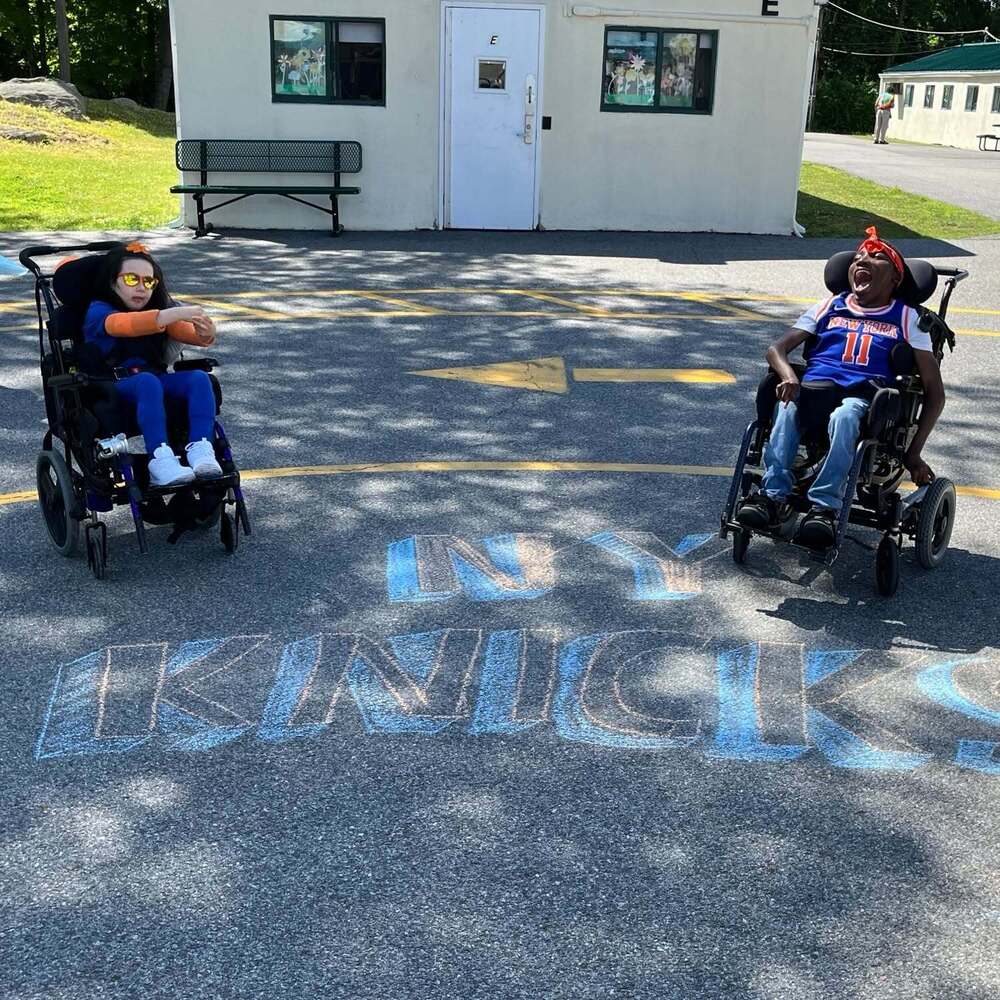 two students in assistive mobile devices sit near NY Knicks chalked on pavement