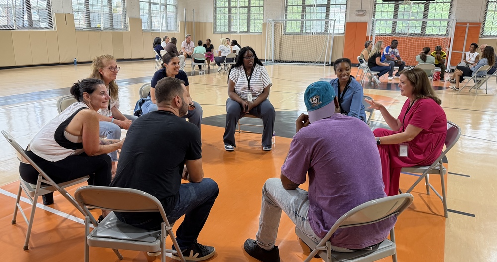 teachers on chairs in a circle in a gym