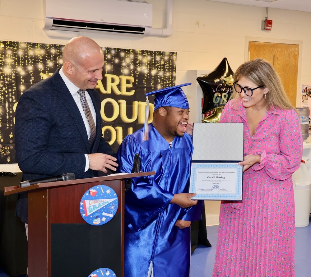 Principal and assistant congratulate happy graduate, holding his diploma