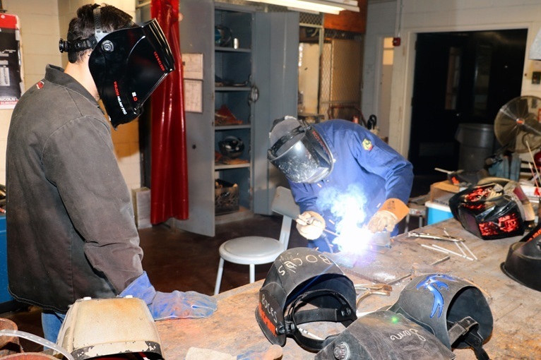 Student watching an instructor demonstrating how to weld