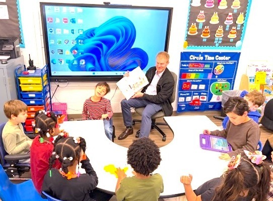 students around a table listen as a parent reads to them