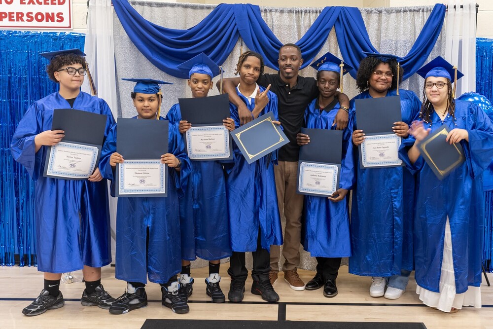 Eighth grade graduates in caps and gowns are joined by their advisor
