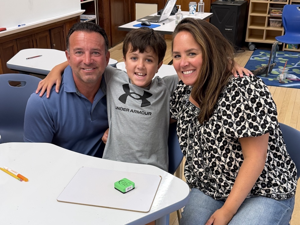 mom and dad embrace son at his desk at school