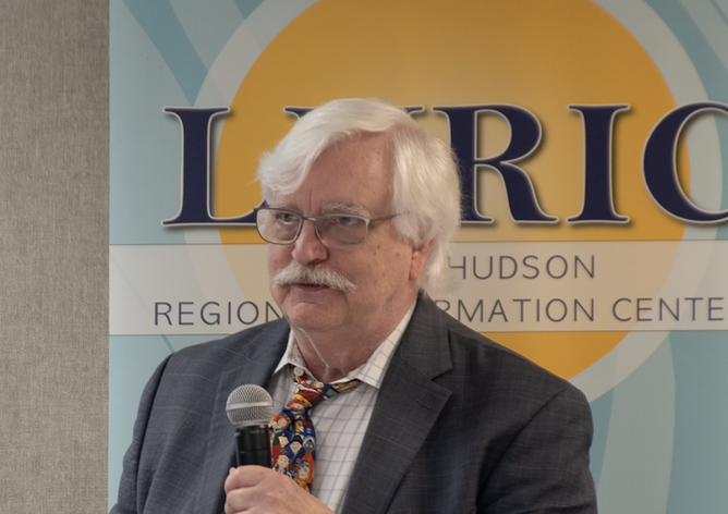 Dr. Chris Dede standing in front of a LHRIC banner
