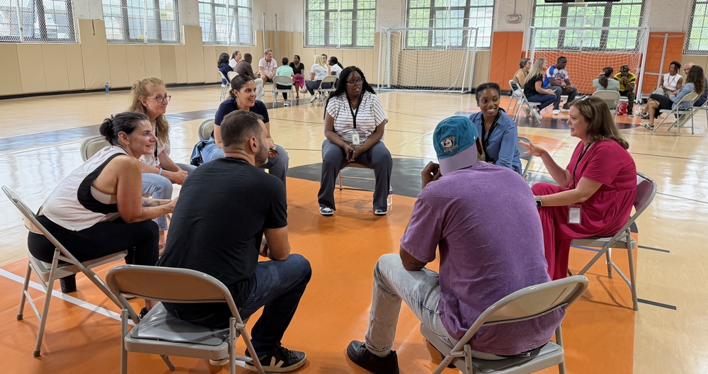 teachers on chairs in a circle in a gym