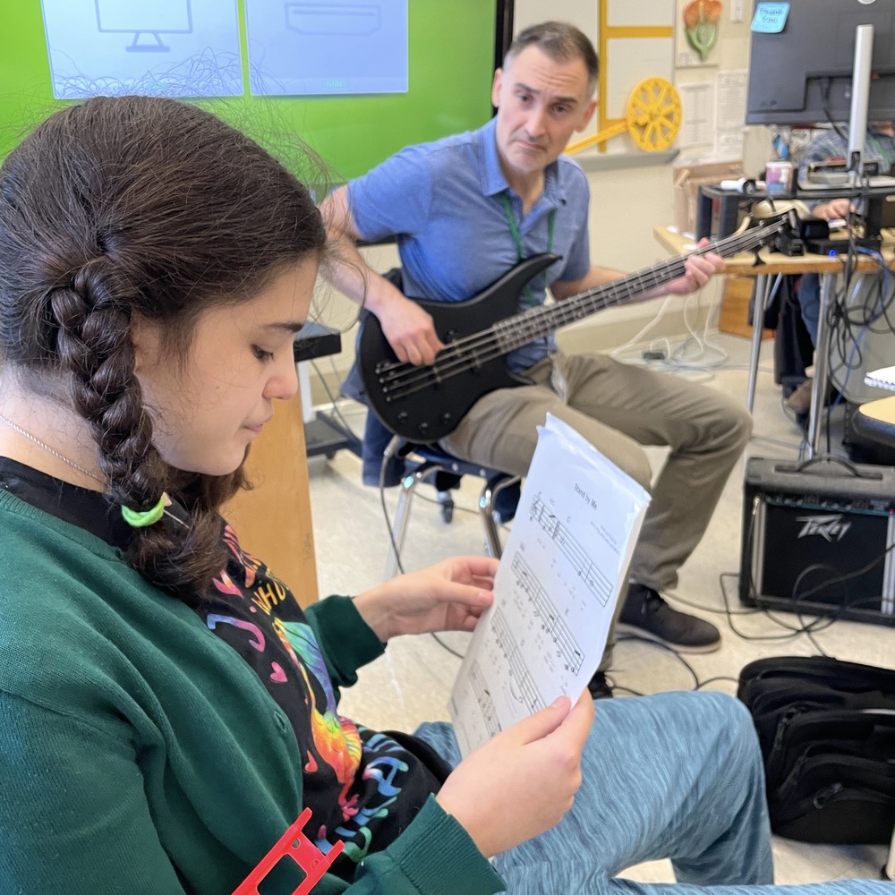 teacher plays bass while watching student sing along