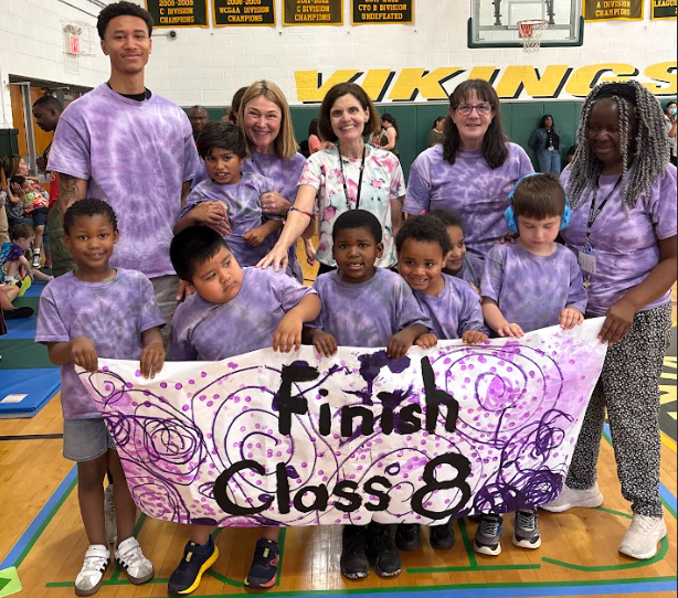 students and teachers in purple tie dyes hold a banner that reads finish class 8