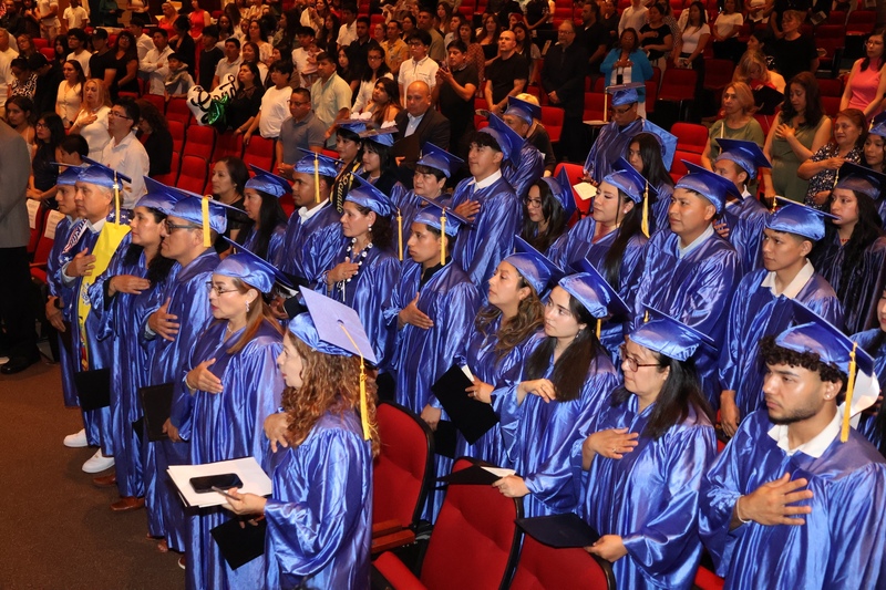 graduates hold hands to heart for anthem