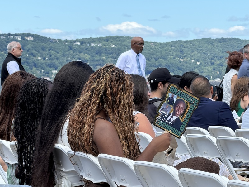 woman at graduation holding sign with graduate's picture on it
