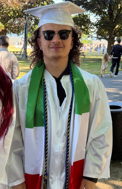 grduate in white cap and gown with multicolored stole