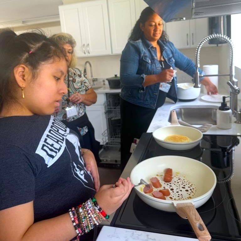 teacher watches as student prepares breakfast on stove