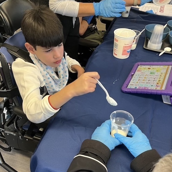 student in wheelchair eats yogurt with teacher's help