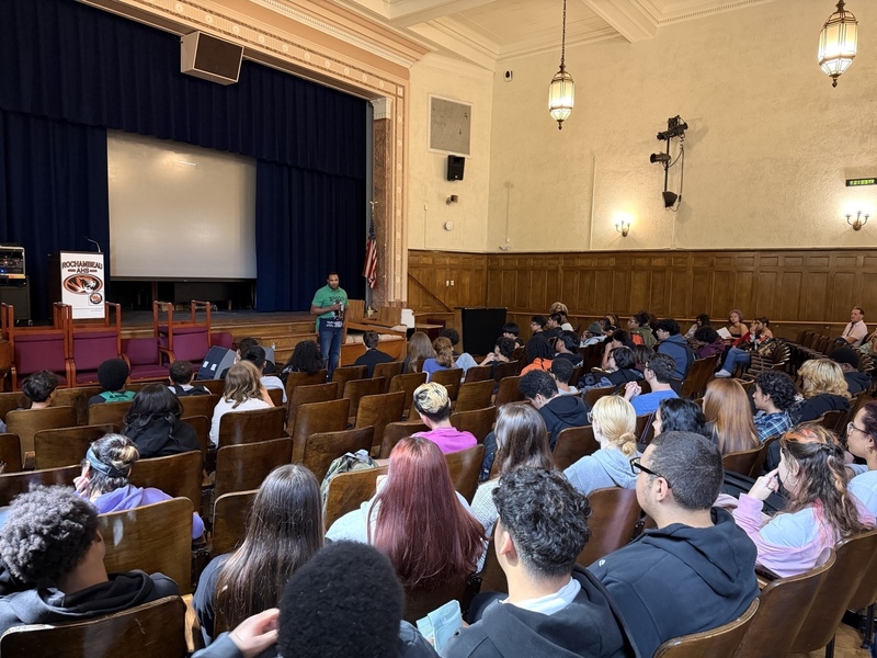 educator leading a student assembly in auditorium