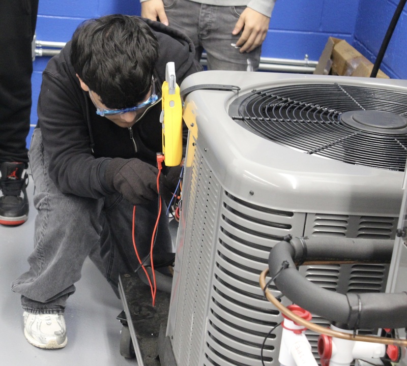 An HVAC student practices on an air conditioning training unit.