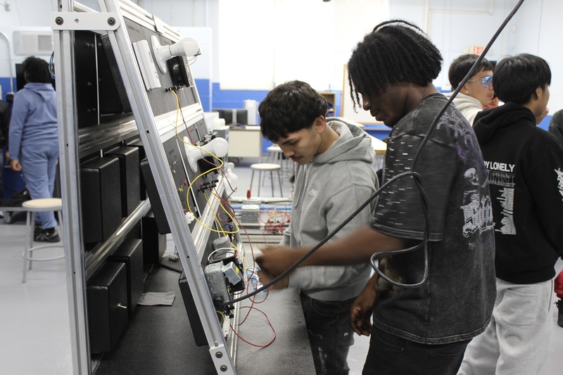 Two HVAC  students prepare a refrigeration training unit.