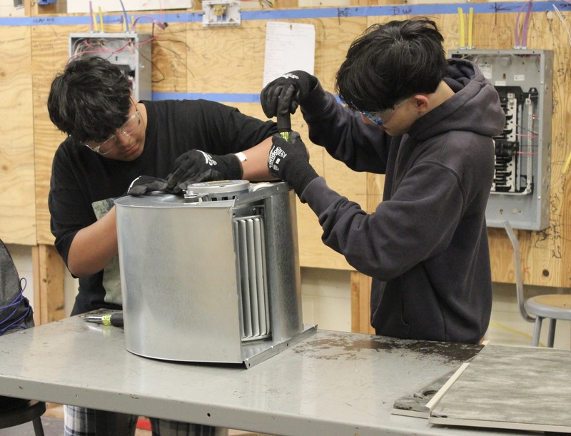 Two HVAC students work on an air conditioning unit.